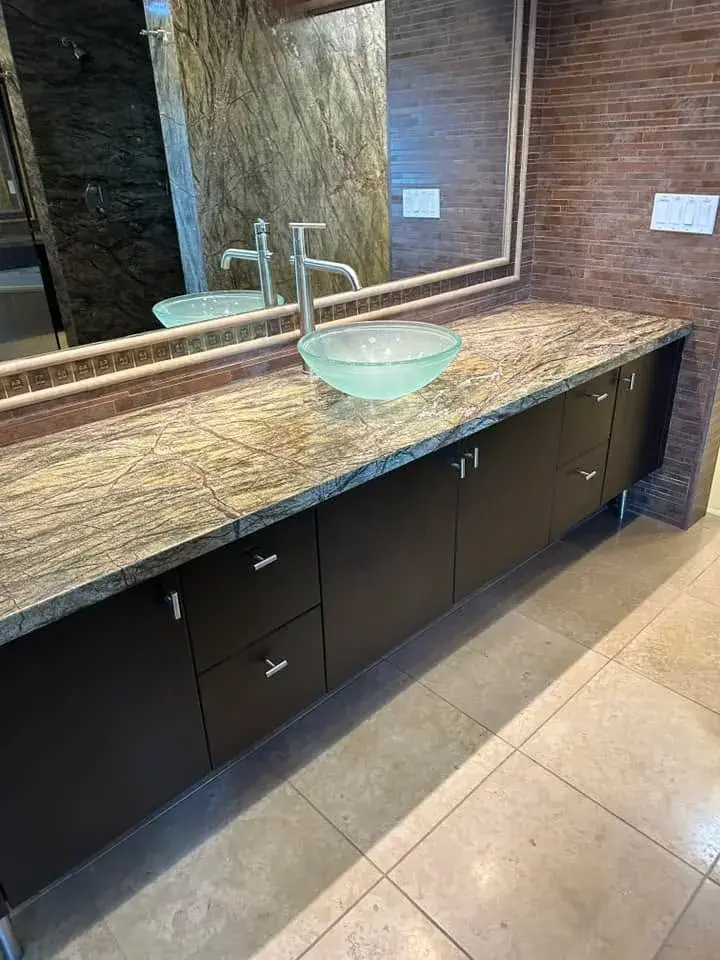 Custom floating vanity with rainforest-marble countertop, dual glass vessel sinks, and brick accent wall by Zona Floors in Arizona