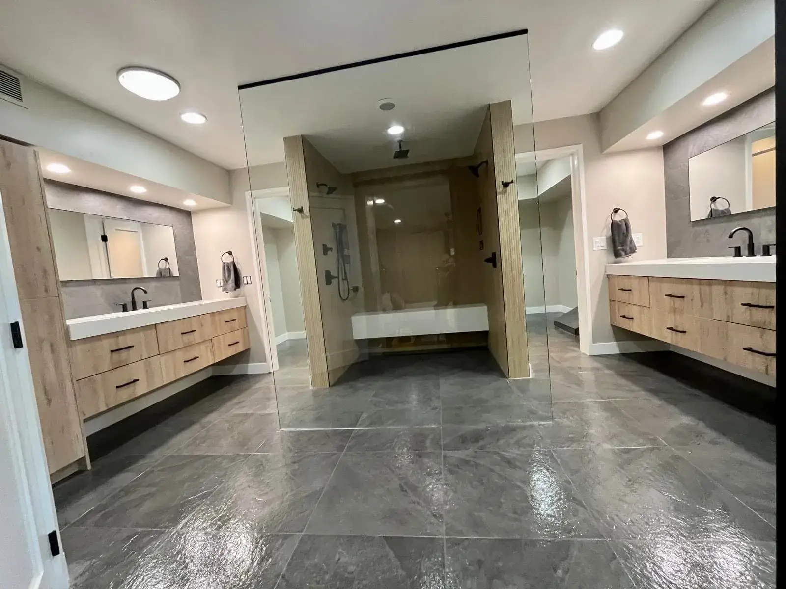 Luxury master bathroom remodel in Arizona by Zona Floors with dual oak vanities flanking a central glass-walled walk-in shower and built-in soaker tub on porcelain tile floors