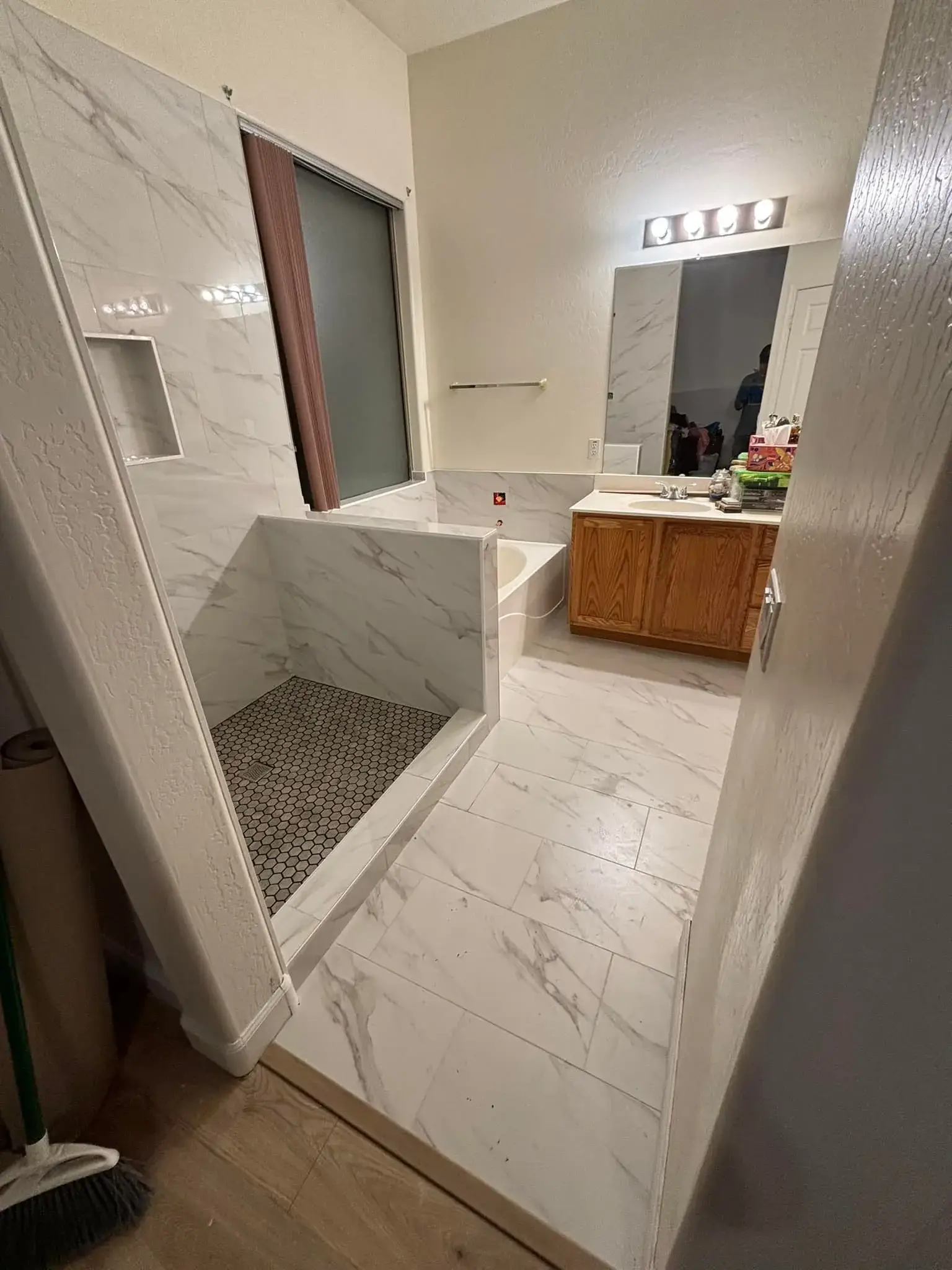 Phoenix master bathroom remodel in progress with full white marble-look porcelain walls, walk-in shower, and oak vanity