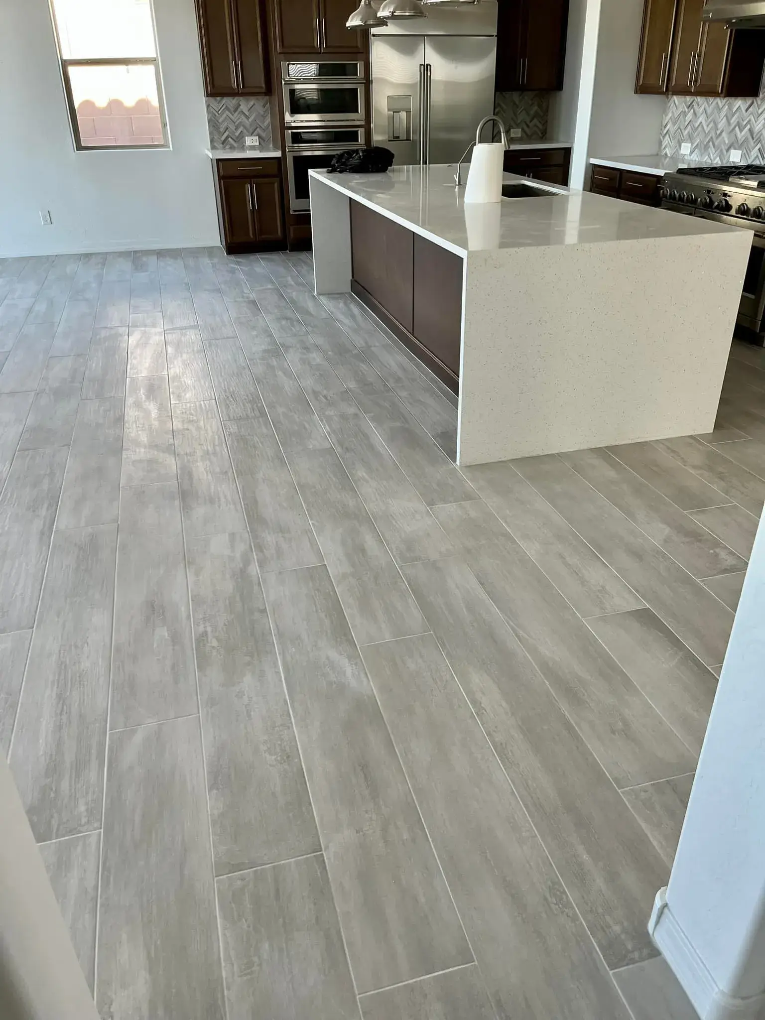 Completed Arizona kitchen with warm wood-look laminate-style flooring, dark cabinets, and white quartz island installed by Zona Floors