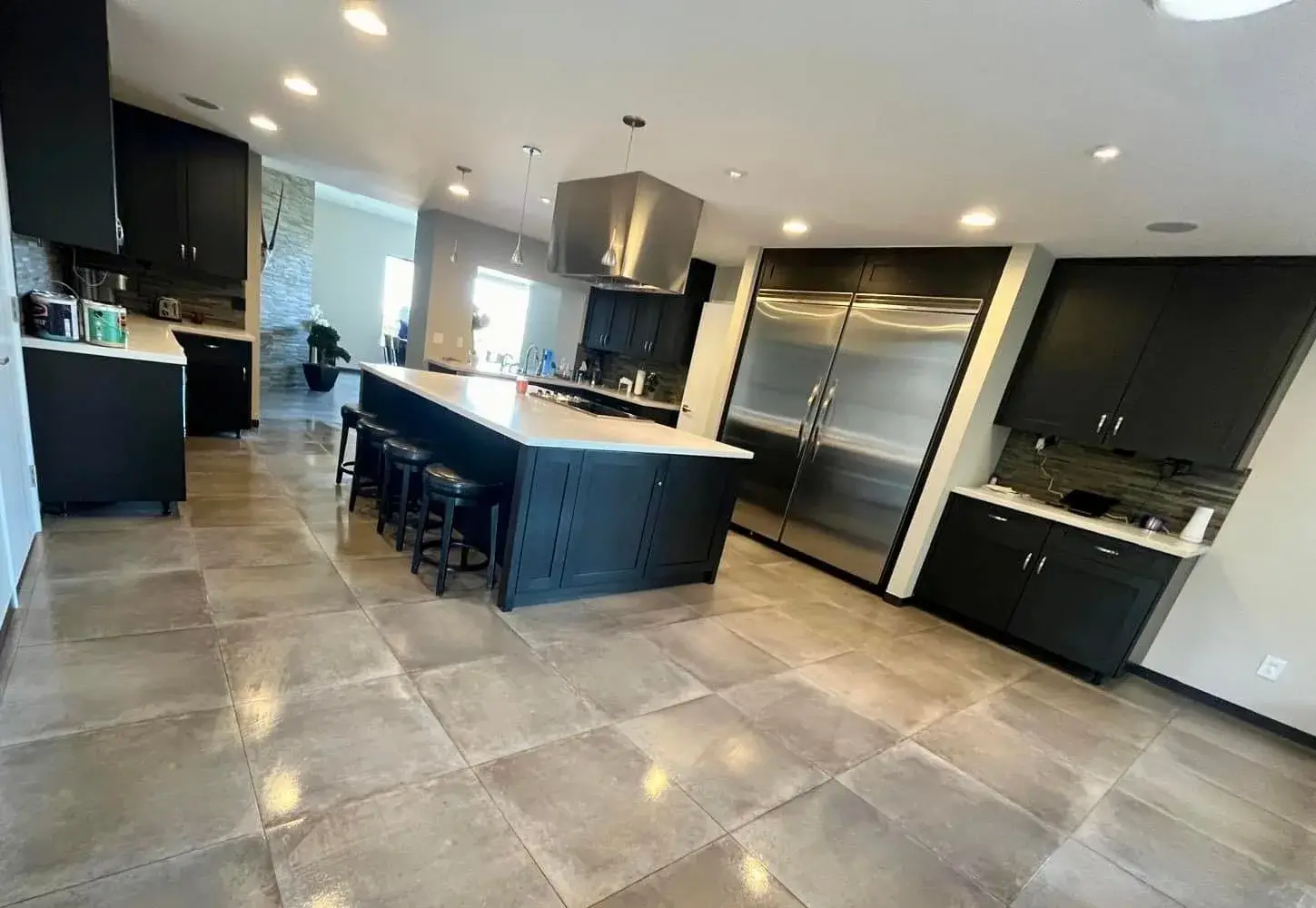 Wide view of a Phoenix-area kitchen remodel with dark navy shaker cabinets, dual stainless built-in refrigerators, large-format porcelain tile floor, and a central island by Zona Floors