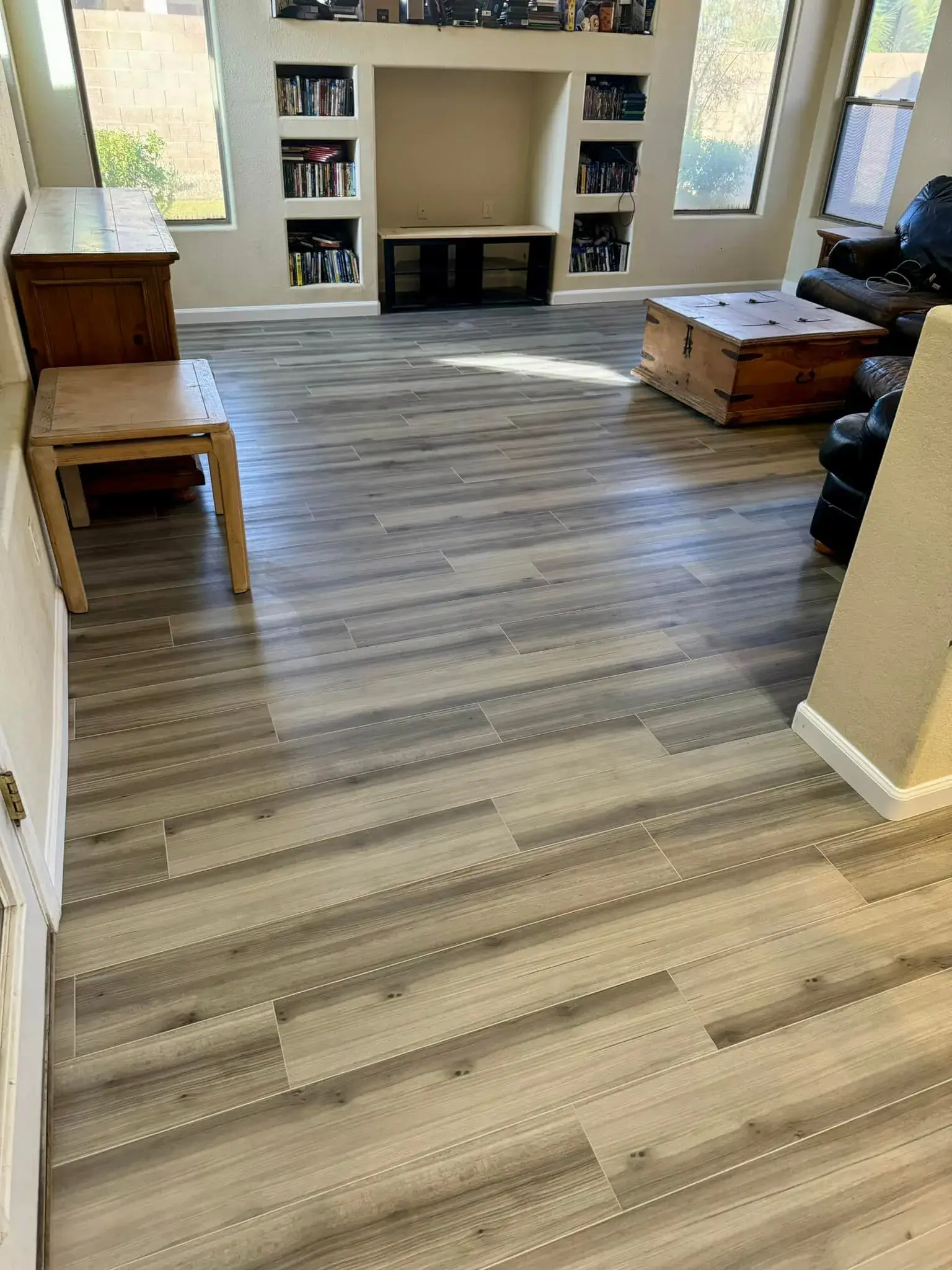 Wood-look luxury vinyl plank flooring in a finished Arizona living room with custom built-in bookshelves and fireplace, installed by Zona Floors