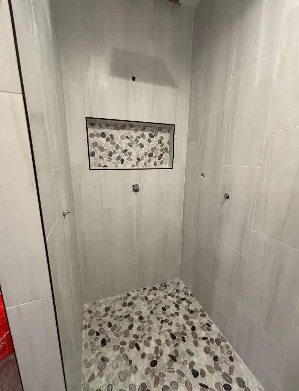 Custom walk-in shower with vertical white subway tile, decorative inset, and pebble-stone shower floor by Zona Floors in Arizona